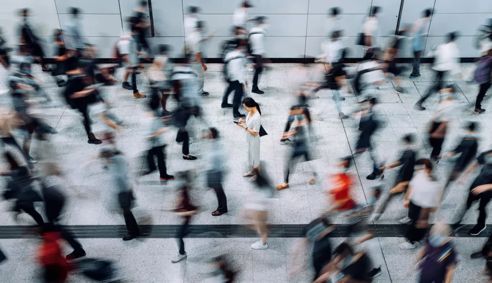 Young woman using smartphone surrounded by commuters rushing by